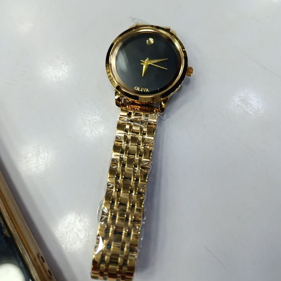 A gold-tone Movado watch with a black dial and gold bracelet, resting on a white surface.