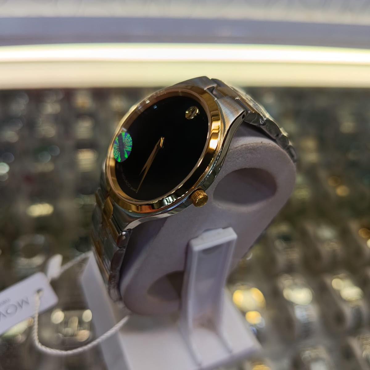A gold-tone and stainless steel smartwatch with a black face and Roman numeral hour markers, displayed on a white stand inside a watch store.