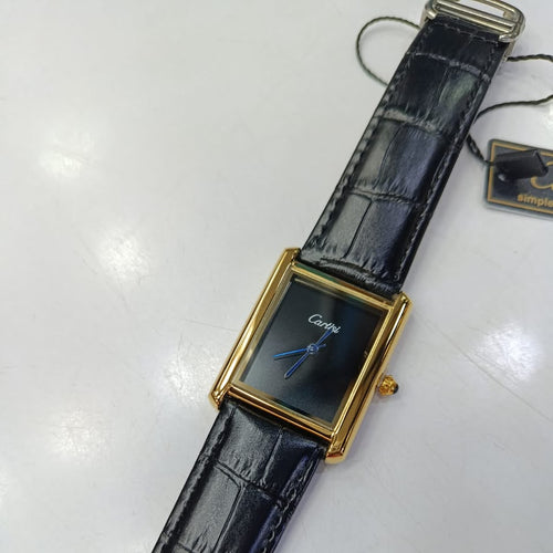 A Cartier watch with a gold-tone rectangular case, black dial, and textured black leather strap, shown on a white surface with a hangtag attached.